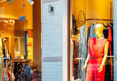 A bright boutique window showcases a red outfit on a mannequin, surrounded by colorful garments on hangers.